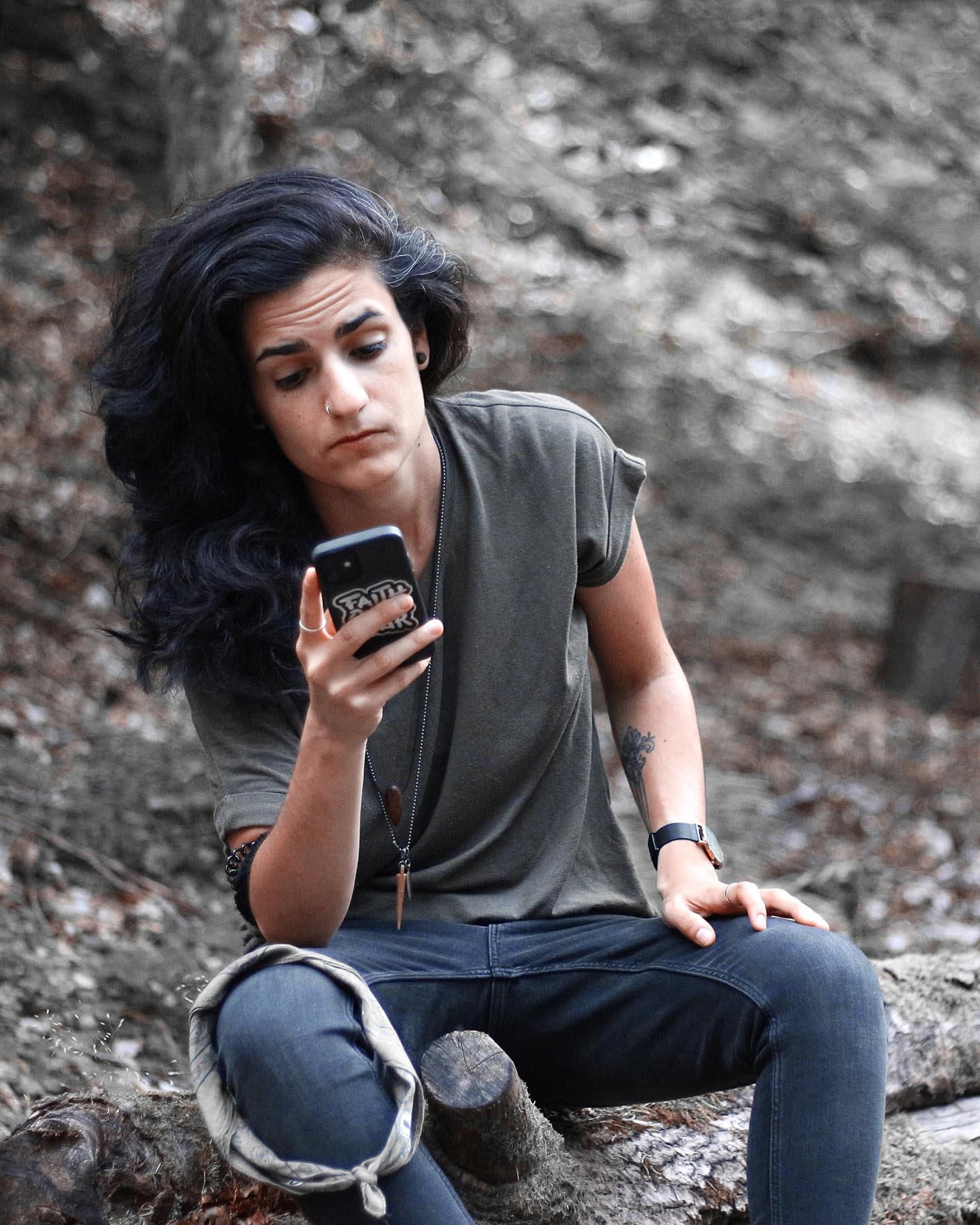 Deniz sitzt im Wald und schaut auf ihr Smartphone um Liebeskummer zu überwinden